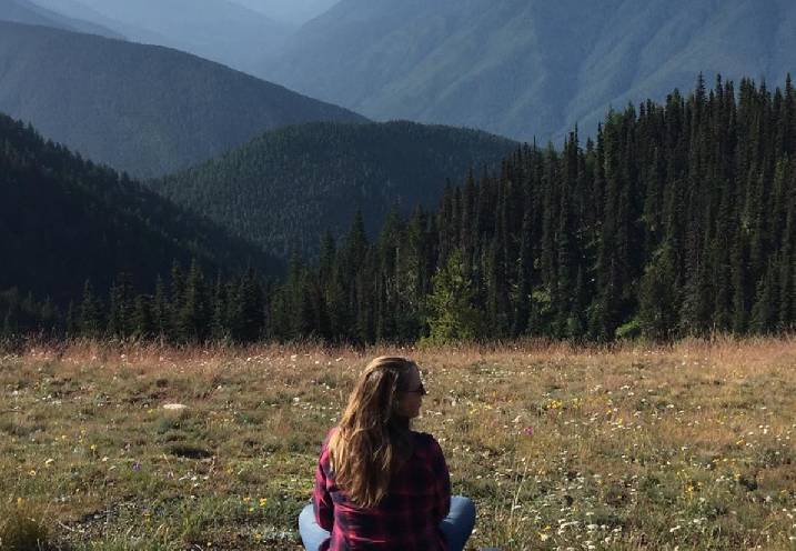 A woman sitting in the grass with mountains behind her.